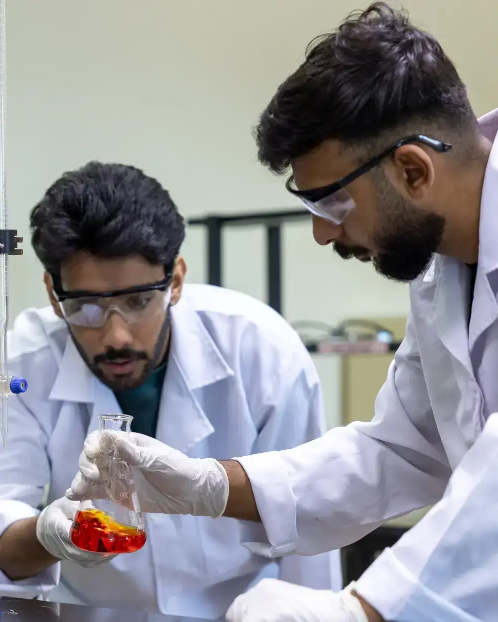 Students in lab coats and safety goggles conducting an experiment at the University of Technology Bahrain
